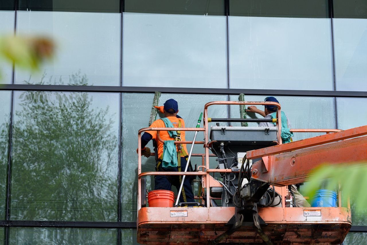 The Art of Drawing Readers In: Your attractive post title goes here Two workers cleaning windows on a glass building facade using a lift platform, enhancing building aesthetics.